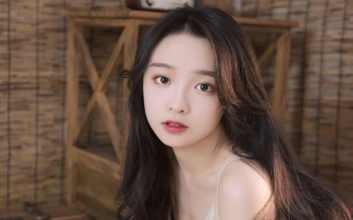一位长发女性面对镜头坐在木质背景前。