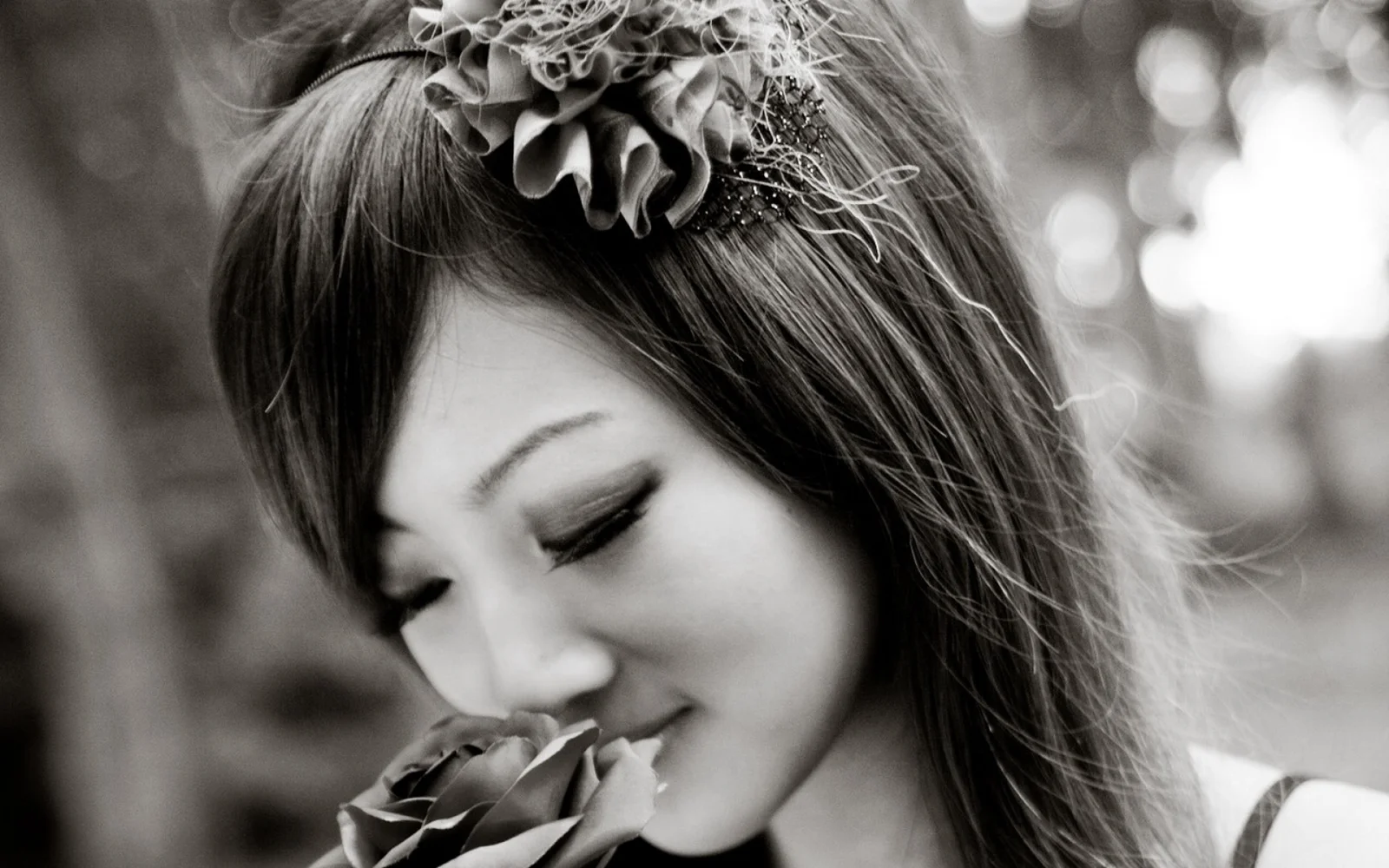 一位成年女性闭眼靠近花朵的黑白侧面人像，背景呈现柔和的户外散景。