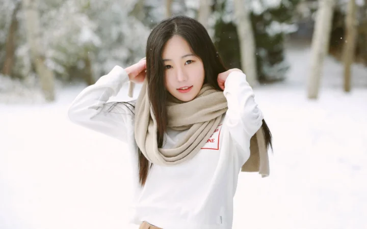 一名长发女子在积雪的户外环境中整理围巾。