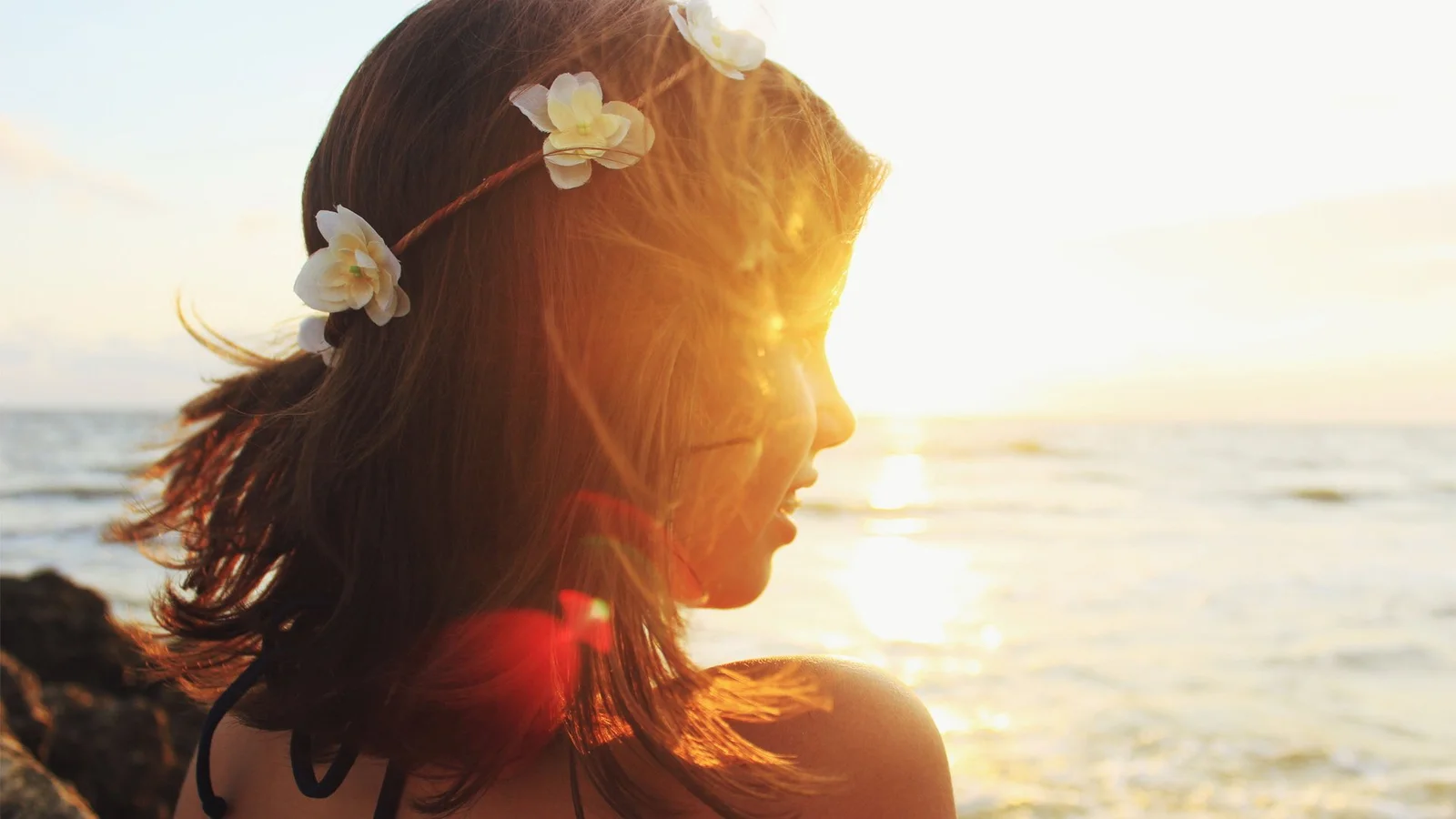 一位戴着花环的女性在海边夕阳下侧身望向海面。