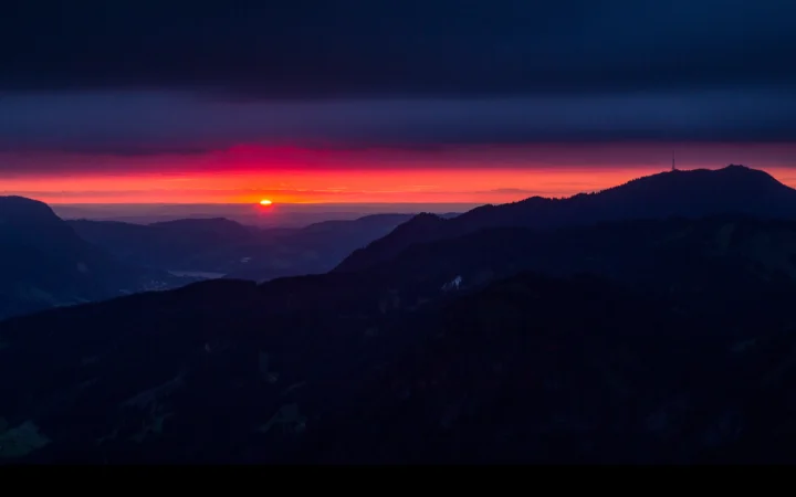 群山剪影映衬着绚丽的夕阳与深蓝色暮空。