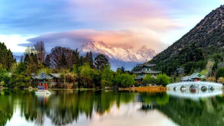 湖面倒映着雪山、树木、亭台和拱桥，构成宁静的山水园林景色。