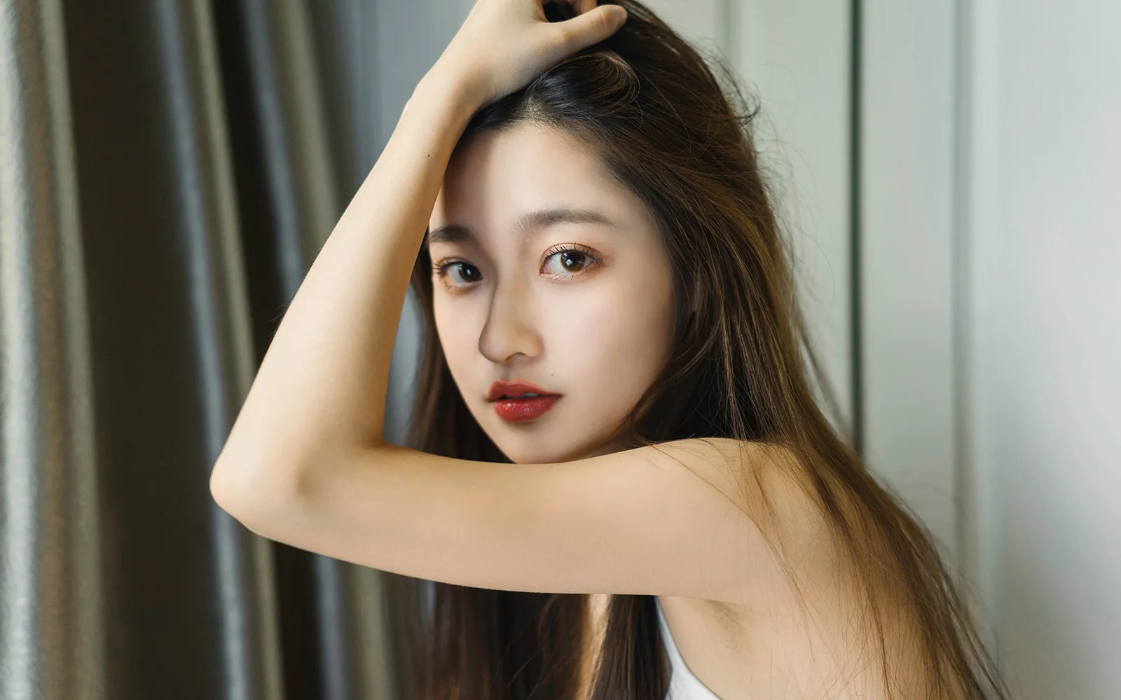 一名长发女性在室内抬手整理头发并看向镜头。