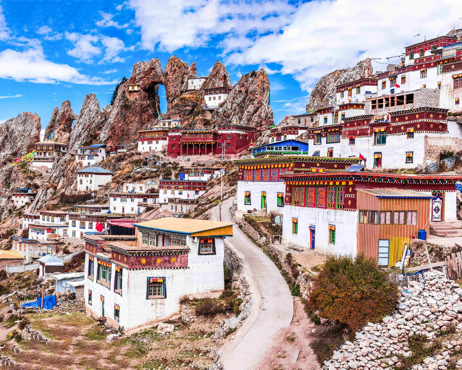 蓝天下，色彩鲜艳的藏式寺院建筑依山而建，周围环绕着陡峭的岩石山峰。