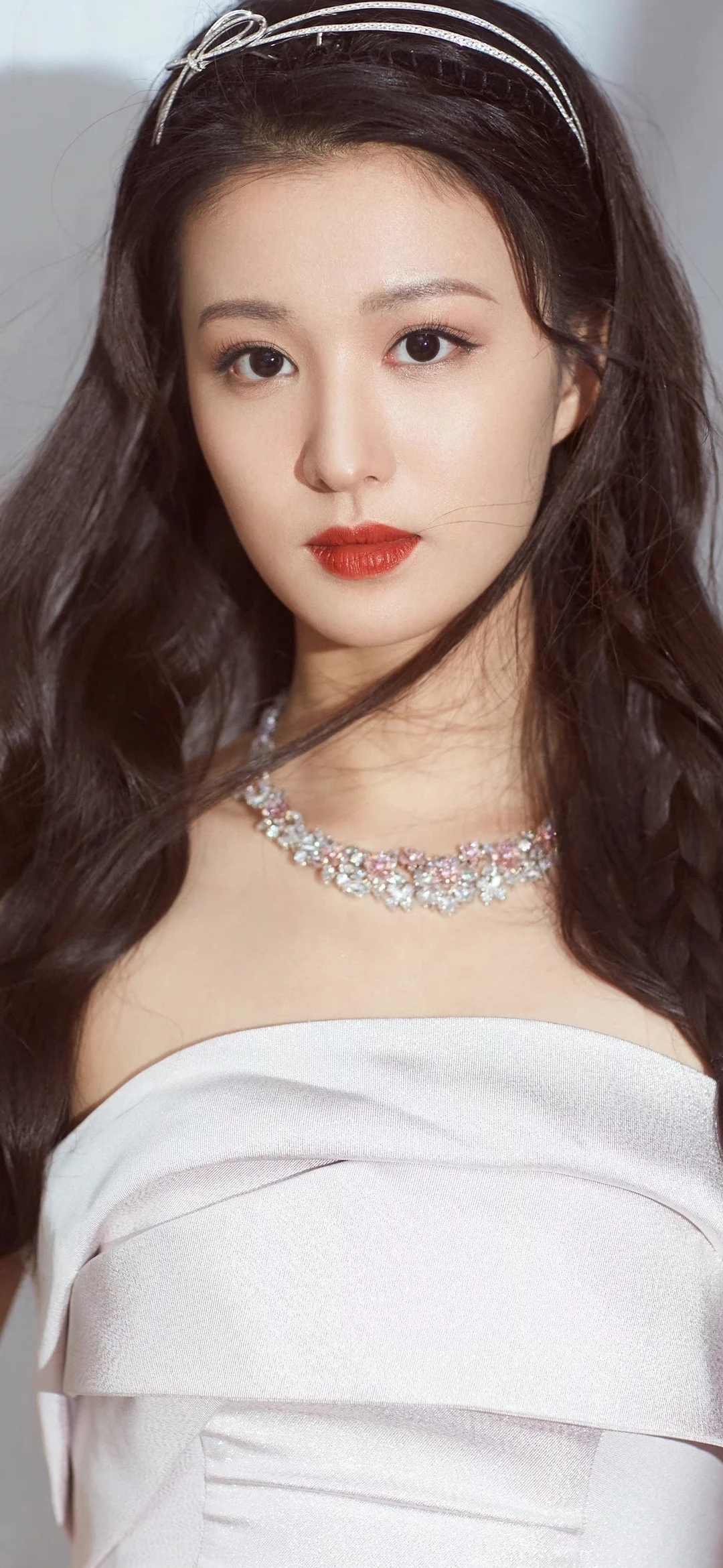 목걸이를 착용한 긴 머리 여성이 흰색 오프숄더 드레스를 입고 카메라를 바라보고 있습니다.