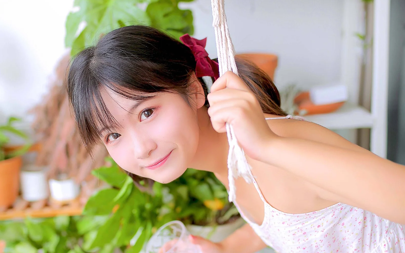 笑顔の女性が室内ブランコに座り、周囲には緑の植物と明るい室内が見えます。