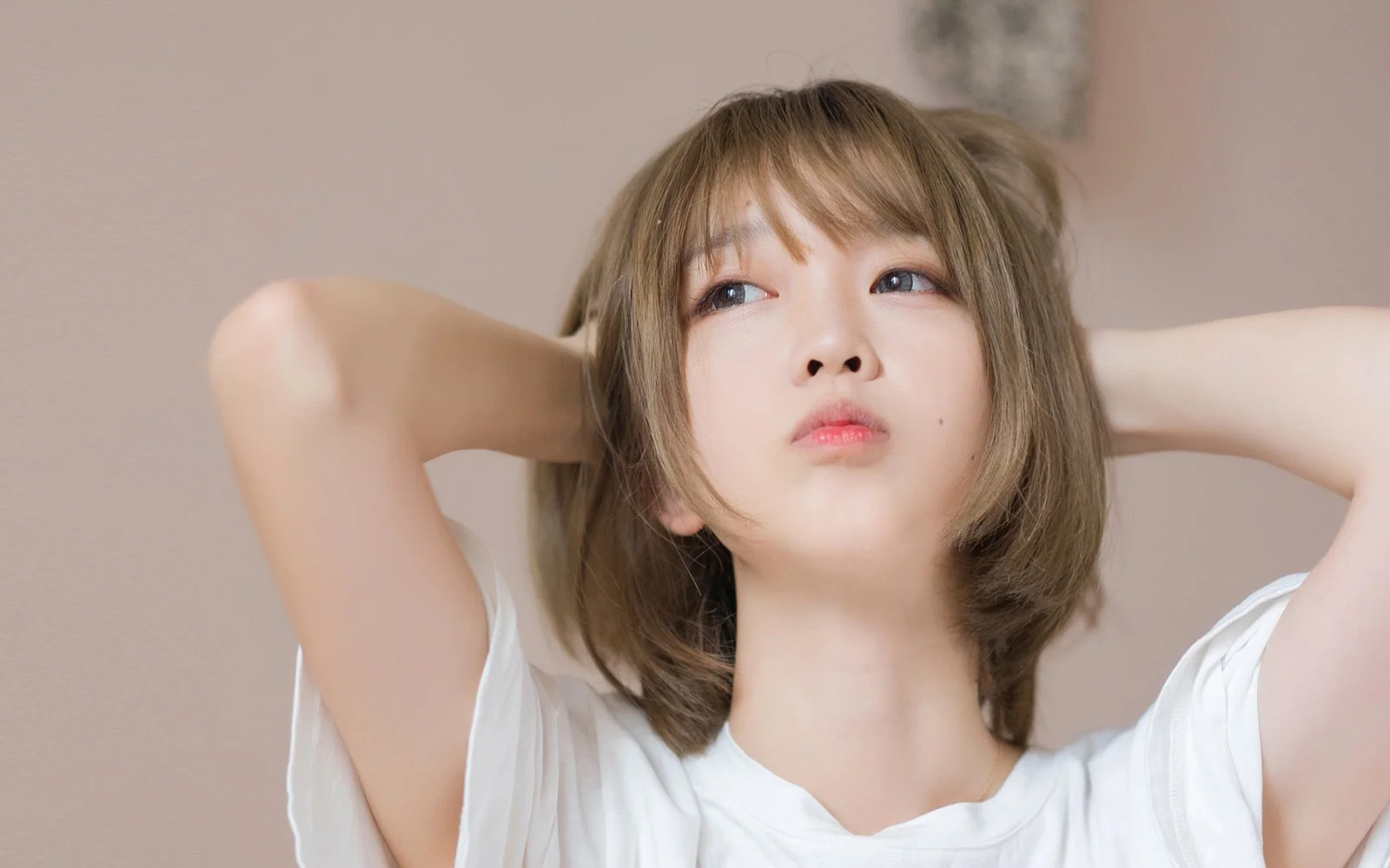 一名短发女性身穿白色上衣，双手置于脑后，面对镜头摆出自然姿态。