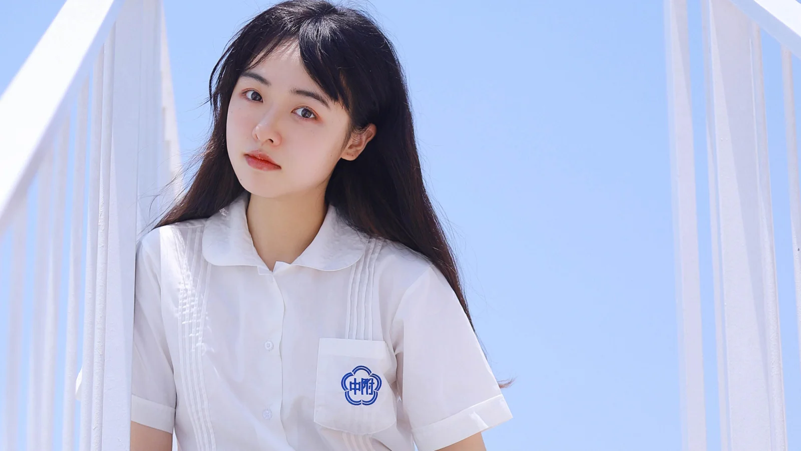 검은 머리의 여성이 푸른 하늘 아래 흰색 다리 구조물 사이에 서 있다.
