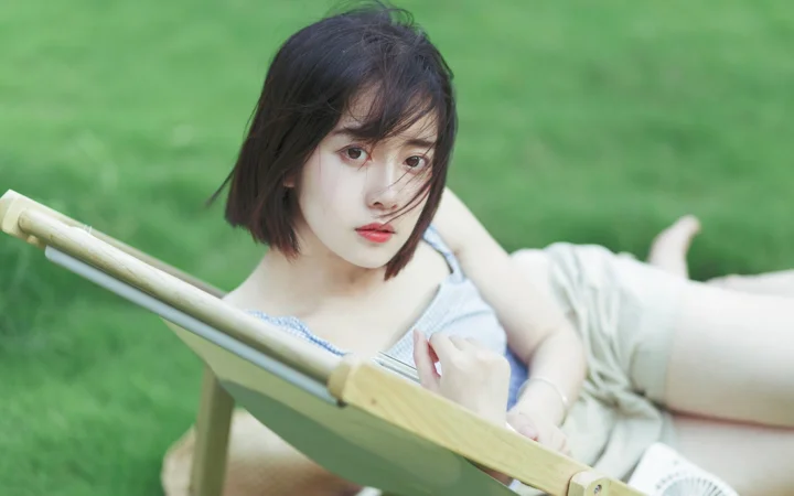 一名女子躺在草地上的木质躺椅中，微风吹动着她的头发。