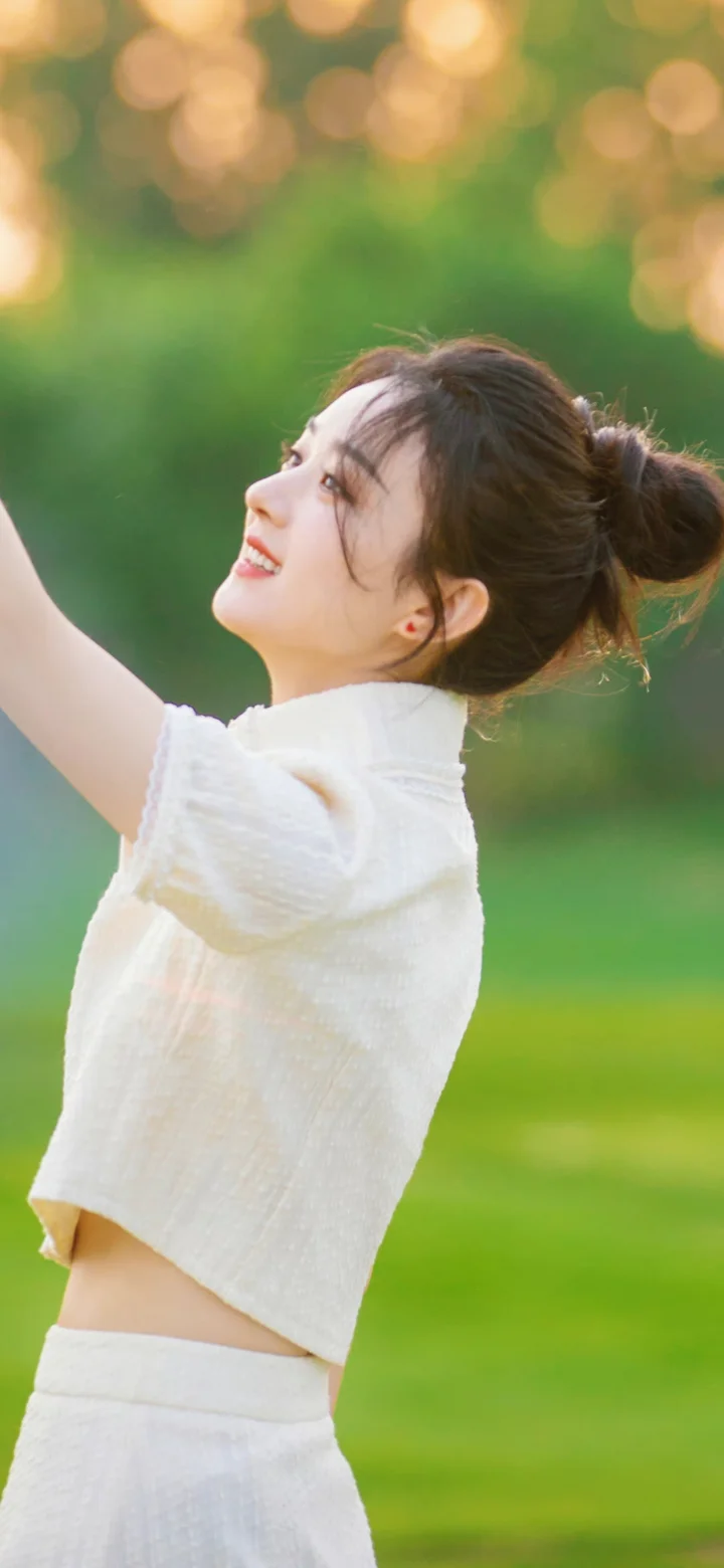 一名身穿白色上衣的女子在绿意背景前抬头微笑。