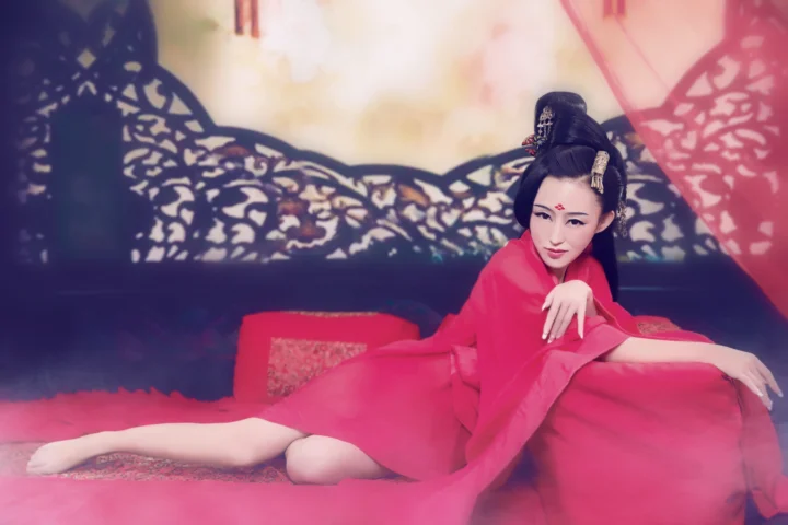 一名身穿鲜粉色传统服饰的女子坐在 ornate 屏风前。