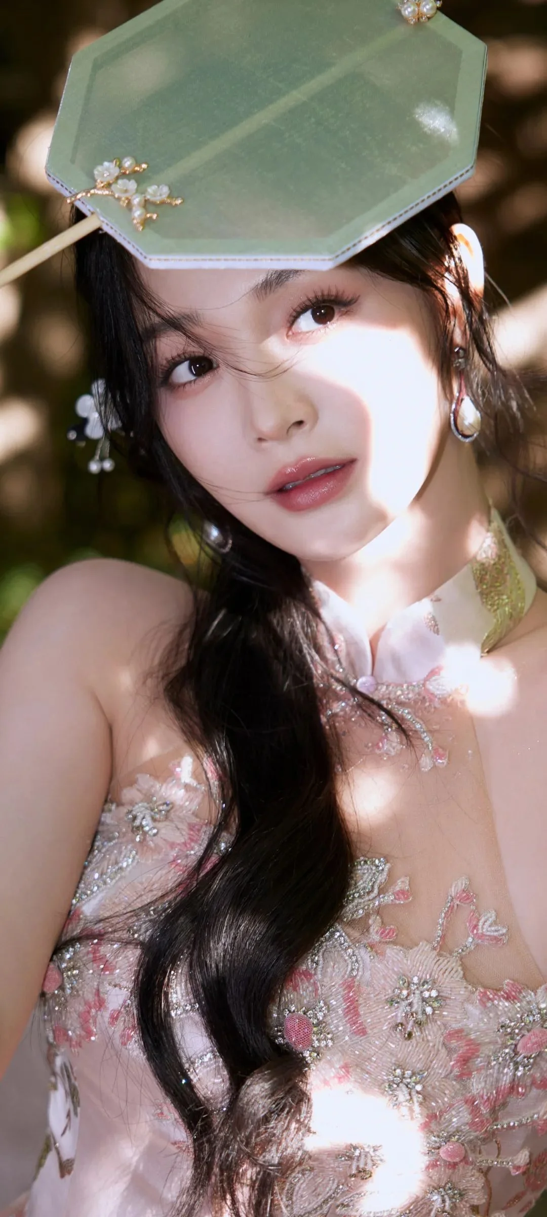 一位長髮女性手持淺綠色花傘，在斑駁光影下身穿淺色花卉裝飾服飾。
