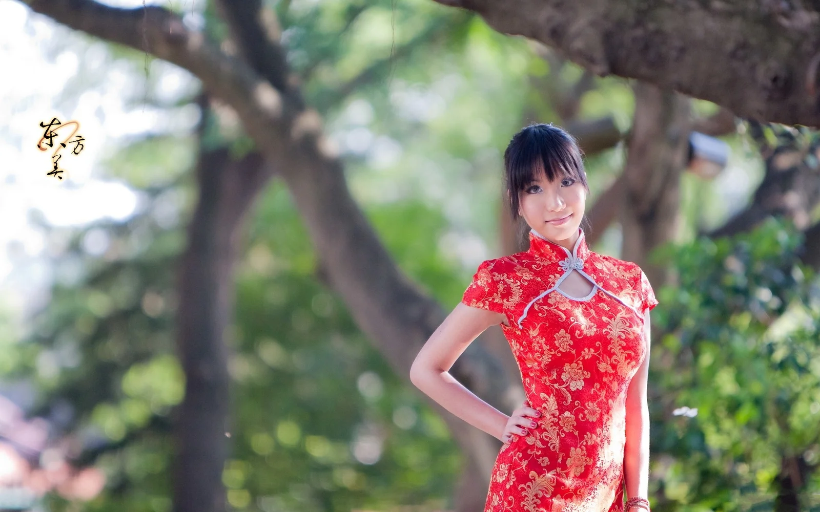 一名成年女子身穿红色旗袍站在绿树掩映的户外环境中。