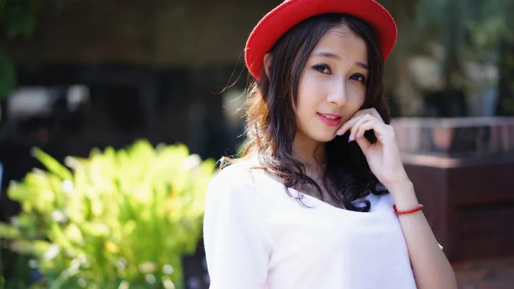 一名戴红色帽子的女性在户外阳光下看向镜头。