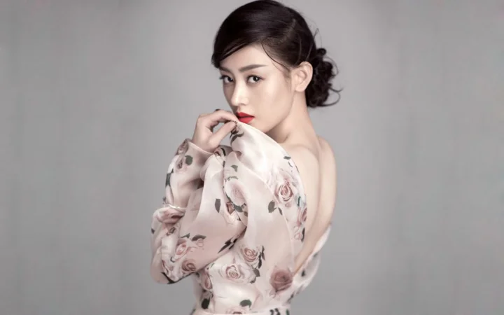 一位成年女性身穿印花上衣，在灰色背景前回眸凝视镜头。