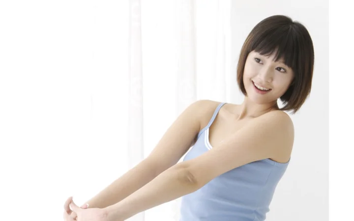 明るい背景の前で、ショートヘアの女性が微笑みながら腕を伸ばしています。