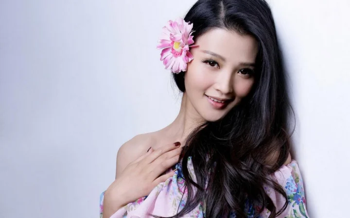 一位戴着粉色花朵、身穿花卉服装的女性在浅色背景前微笑。