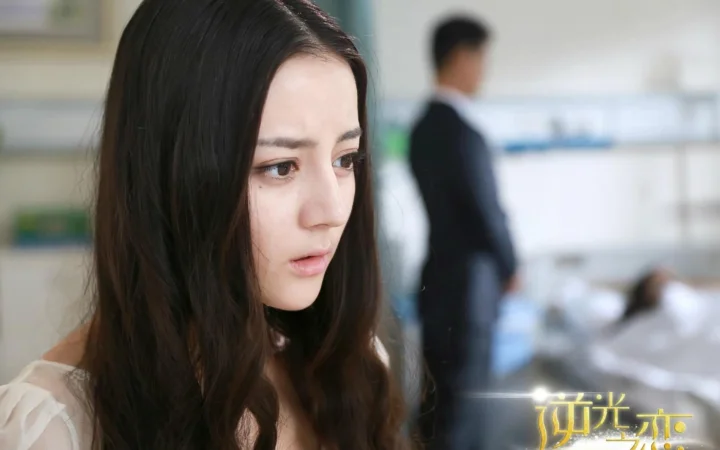 一名成年女性的面部近景侧脸，背景中有一位模糊的人影。