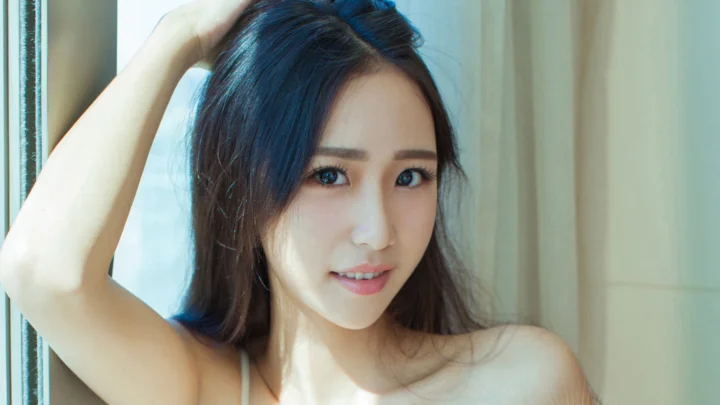 창가에서 한 여성이 한쪽 팔을 올리고 카메라를 향해 미소 짓고 있다.