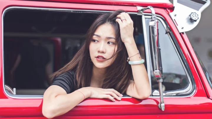 一名女子靠在红色汽车的车窗边，手扶着头发望向一侧。