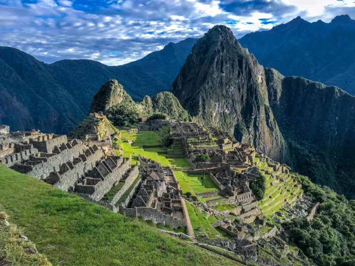 群山环抱中的古代石砌遗址坐落在翠绿山谷之间，天空覆盖着层叠的云朵。