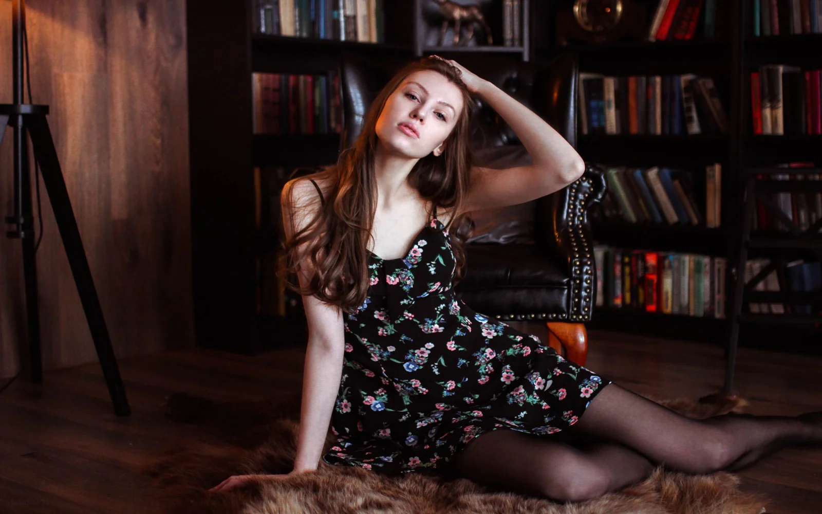 一名穿着黑色碎花连衣裙的女子坐在书架环绕的室内空间中。