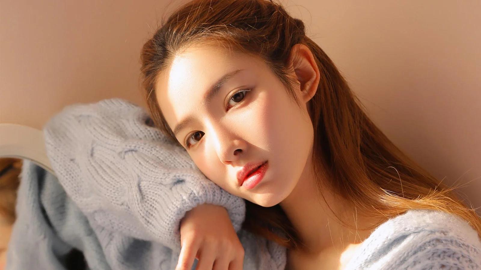 밝은 색 니트 스웨터를 입은 갈색 머리 여성이 카메라 가까이에서 부드러운 인물 사진을 보여줍니다.