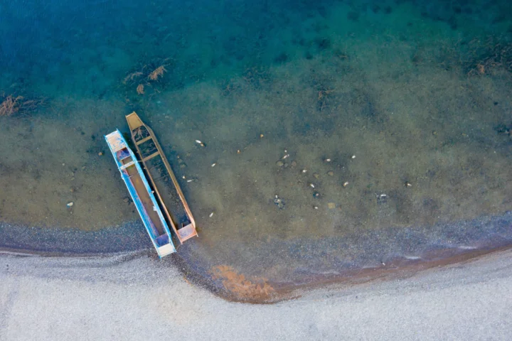 俯视角度呈现清澈海水、沙滩海岸线和停靠在岸边的两艘小船。