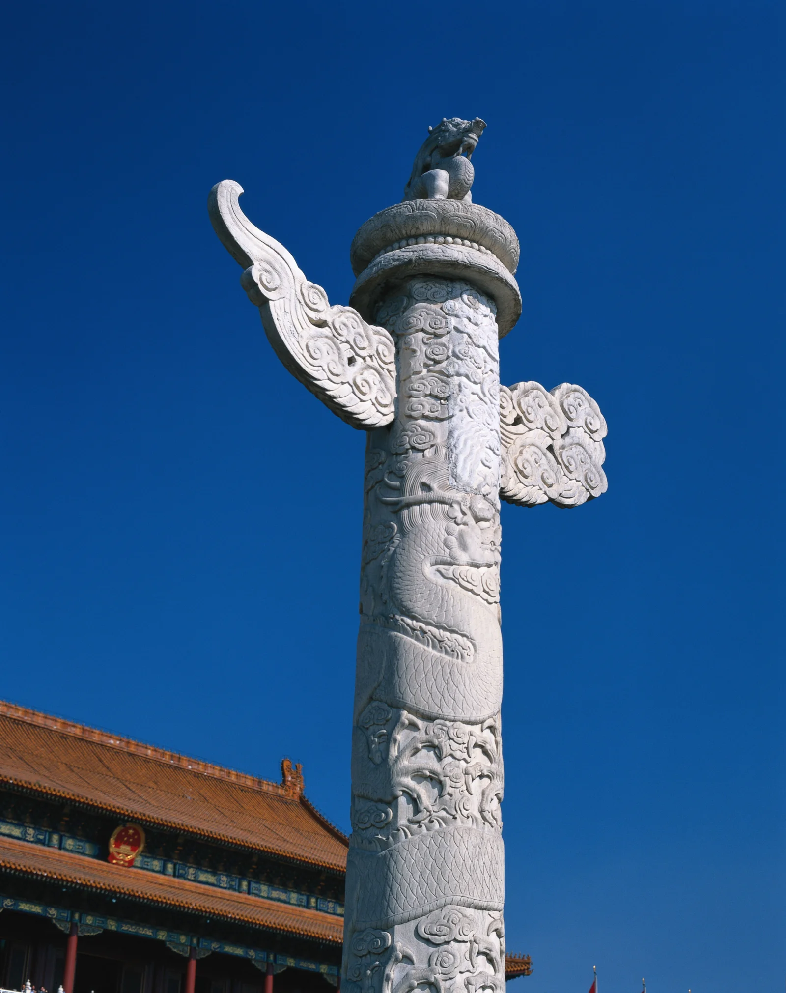 雕刻精美的石柱矗立在蓝天下，旁边是一座传统中式建筑。