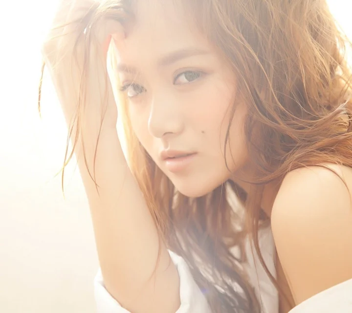 柔和暖光下，一位长发女性以近距离侧脸姿态面对镜头。