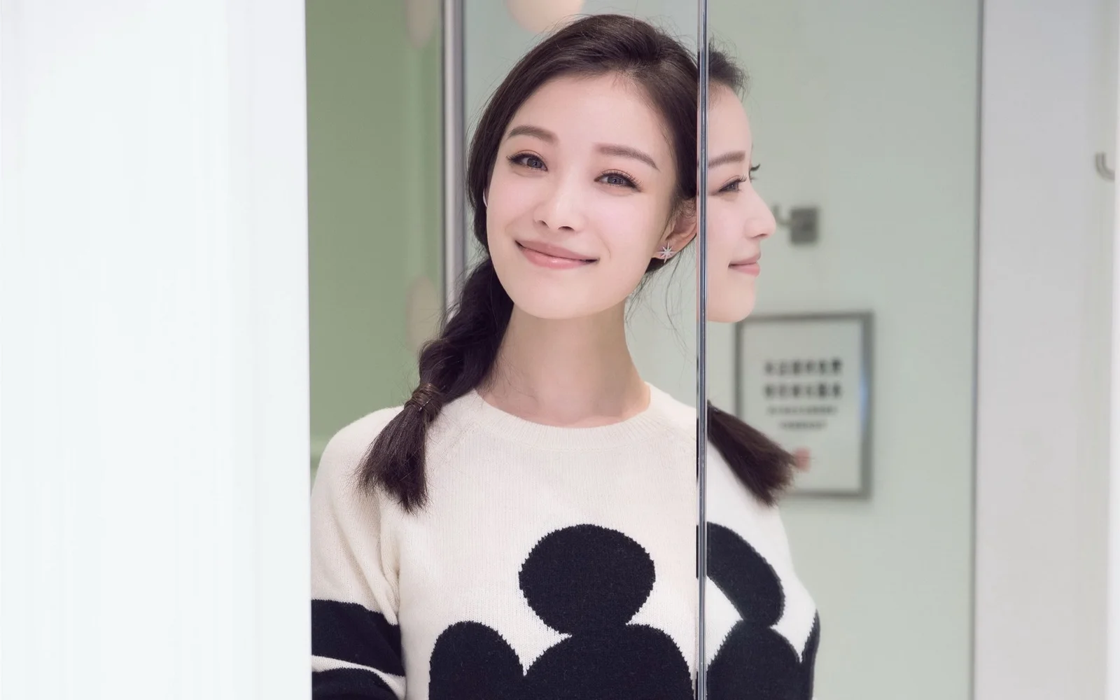 一位成年女性对着镜头微笑，旁边映出她在镜中的侧面倒影。