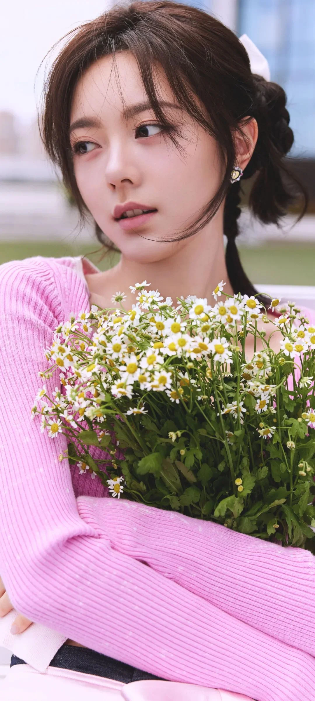 ピンクのニットを着た女性が、白い小さな花の大きな花束を抱えている。