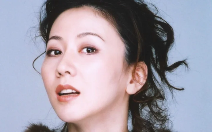 연한 청회색 배경을 뒤로하고 검은 머리를 묶은 성인 여성의 얼굴을 담은 클로즈업 초상입니다.