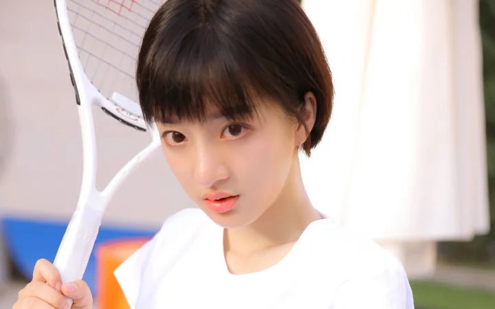짧은 머리의 여성이 흰색 상의를 입고 흰색 테니스 라켓을 든 클로즈업 인물 사진입니다.