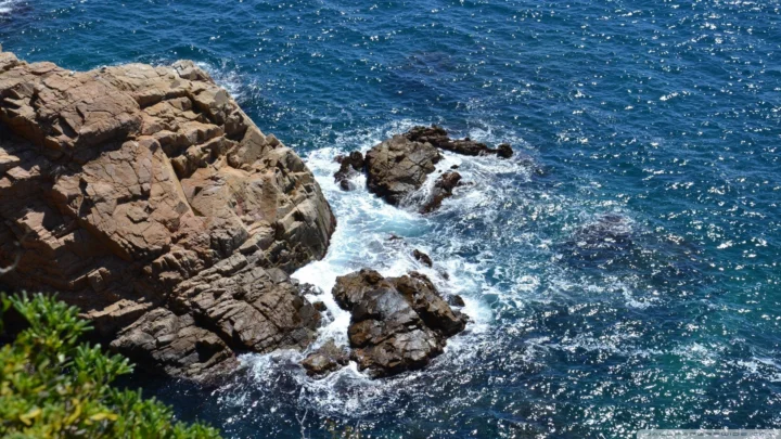 阳光下的蓝色海水拍打着崎岖的岩石海岸。