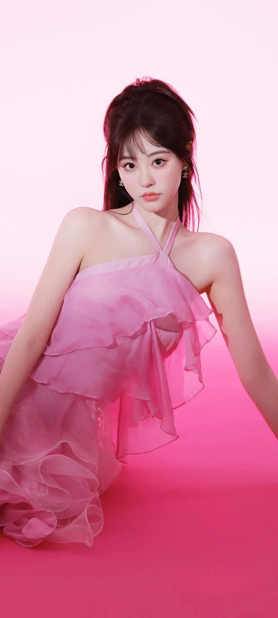 ピンクの重ねドレスを着た女性が、ピンクの背景の前でポーズを取っています。