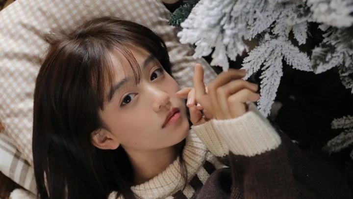一名女性穿着针织毛衣，靠在覆霜圣诞树旁看向镜头。