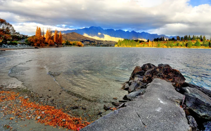 湖水、秋色树木、远山与岸边岩石构成宁静的自然风景。