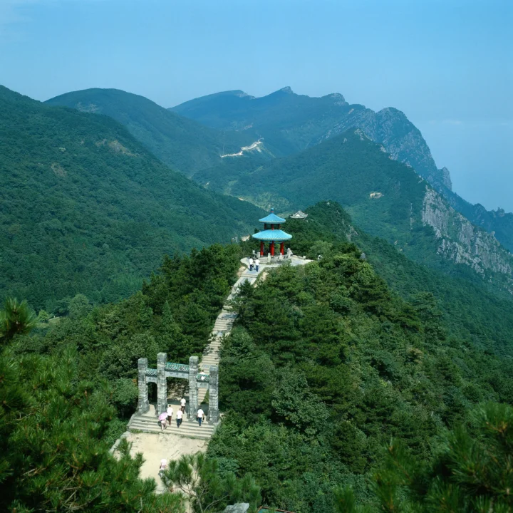 一座山亭坐落在茂密森林间的山脊步道上，远处是层叠的青山与峭壁。