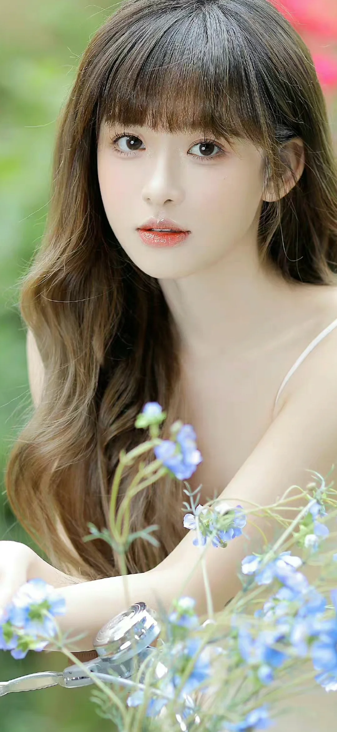 긴 머리의 여성이 파란 꽃을 들고 있는 클로즈업 인물 사진입니다.