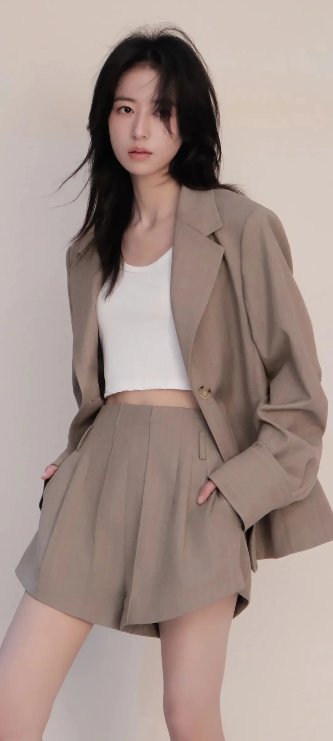 밝은 색 배경 앞에 회갈색 블레이저와 반바지를 입은 성인 여성이 서 있습니다.