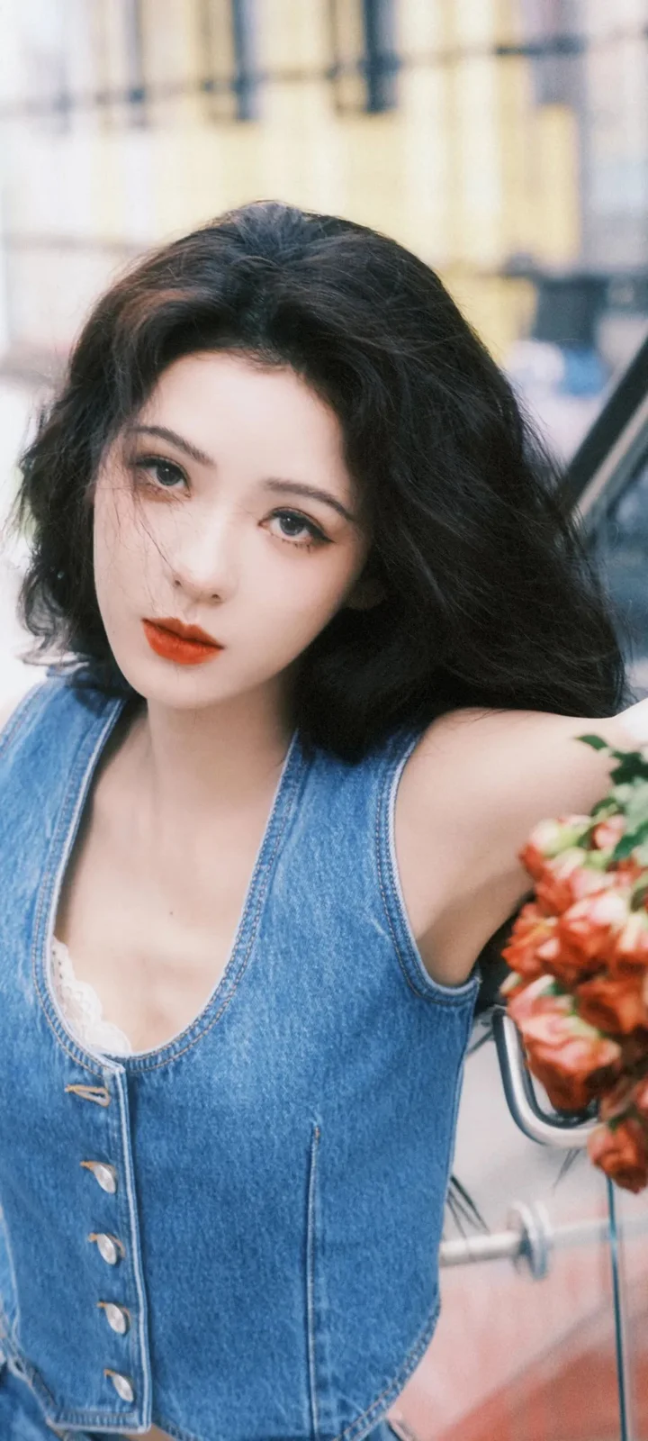 一位成年女性身穿蓝色牛仔背心，在城市背景前面对镜头。