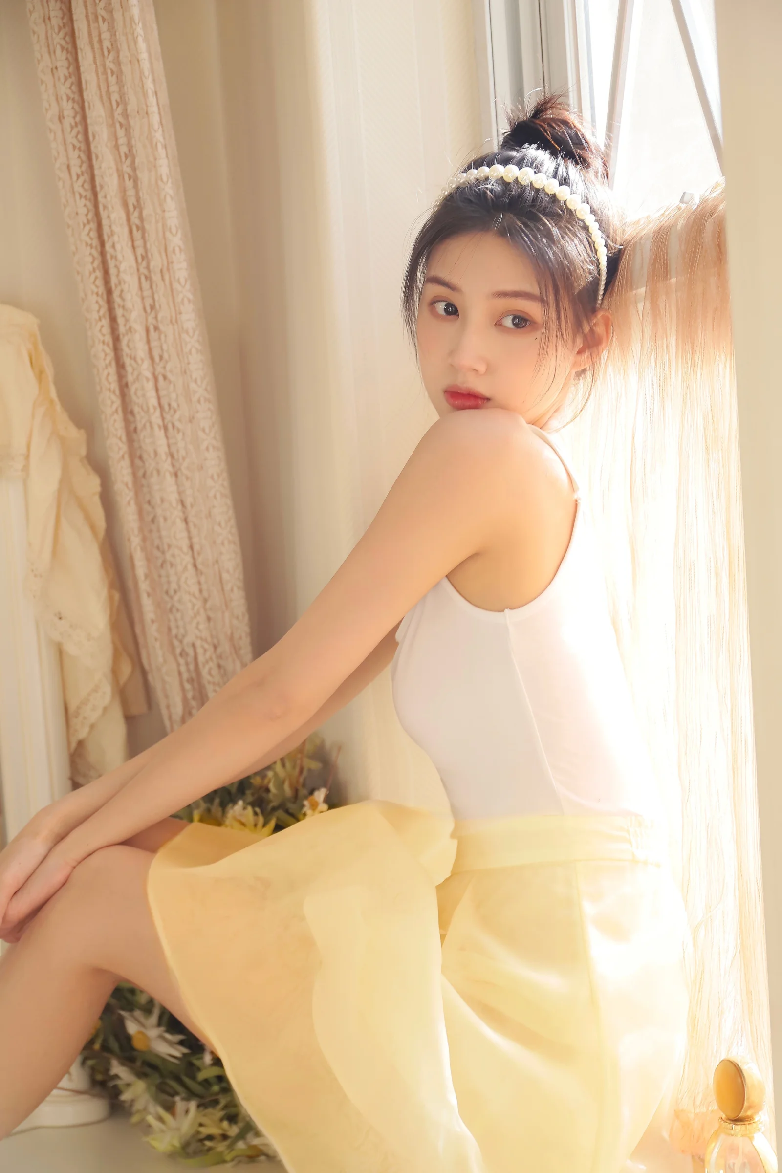 一名身穿白色上衣和黄色裙子的女性坐在窗边，沐浴在柔和的暖色阳光中。