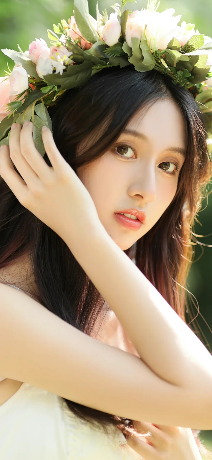 一位戴着花冠的成年女性在绿色户外背景前摆 pose。
