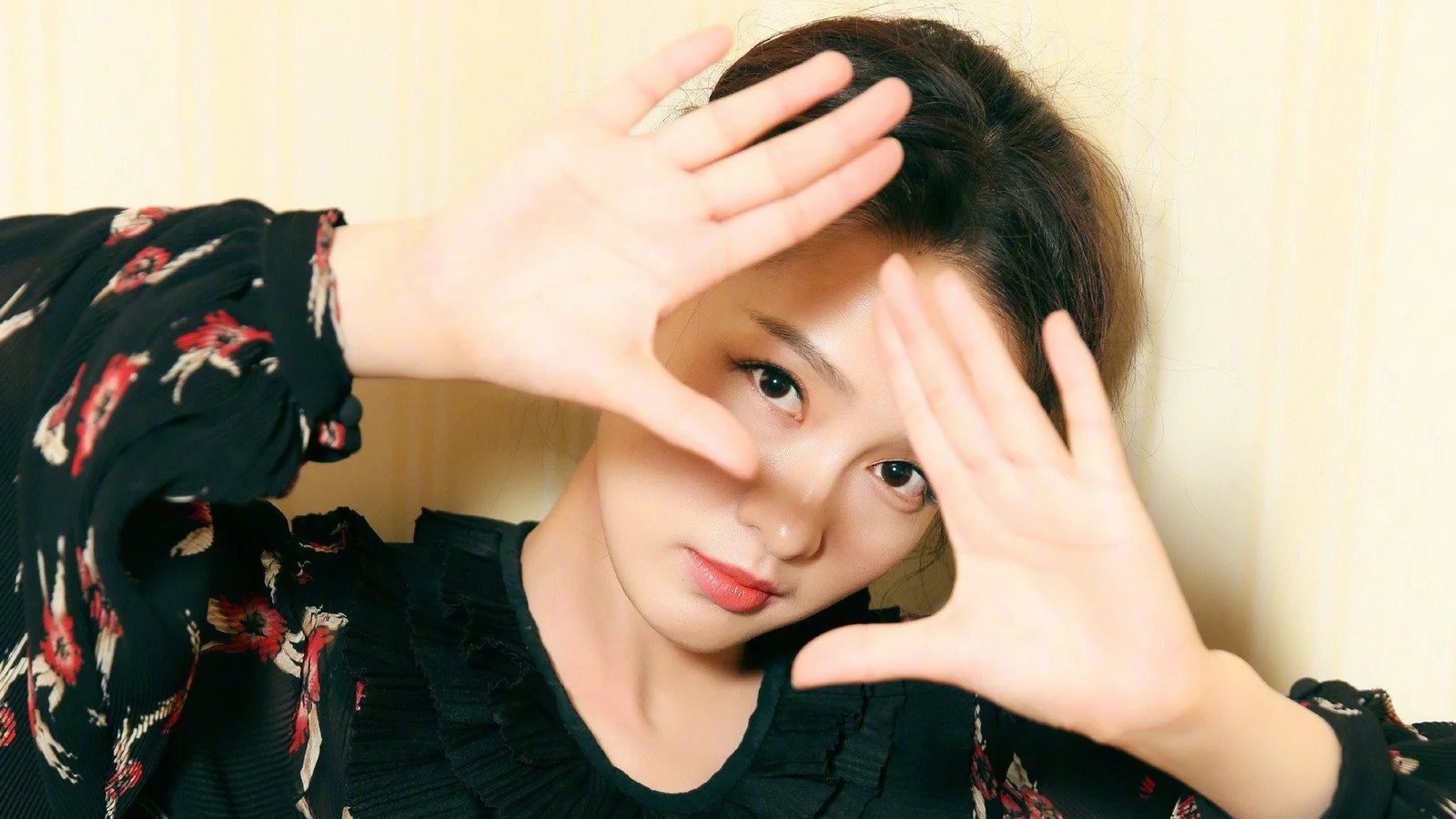 한 여성이 카메라를 가까이 바라보며 얼굴 옆에서 양손으로 프레임 같은 포즈를 취하고 있습니다.