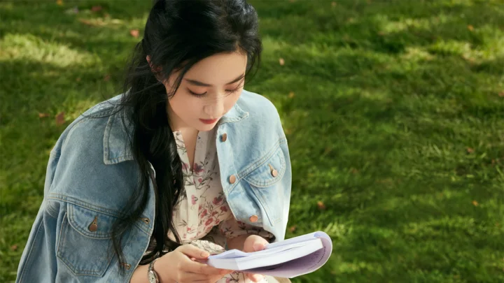 한 여성이 잔디밭에 앉아 고개를 숙이고 책을 읽고 있습니다.