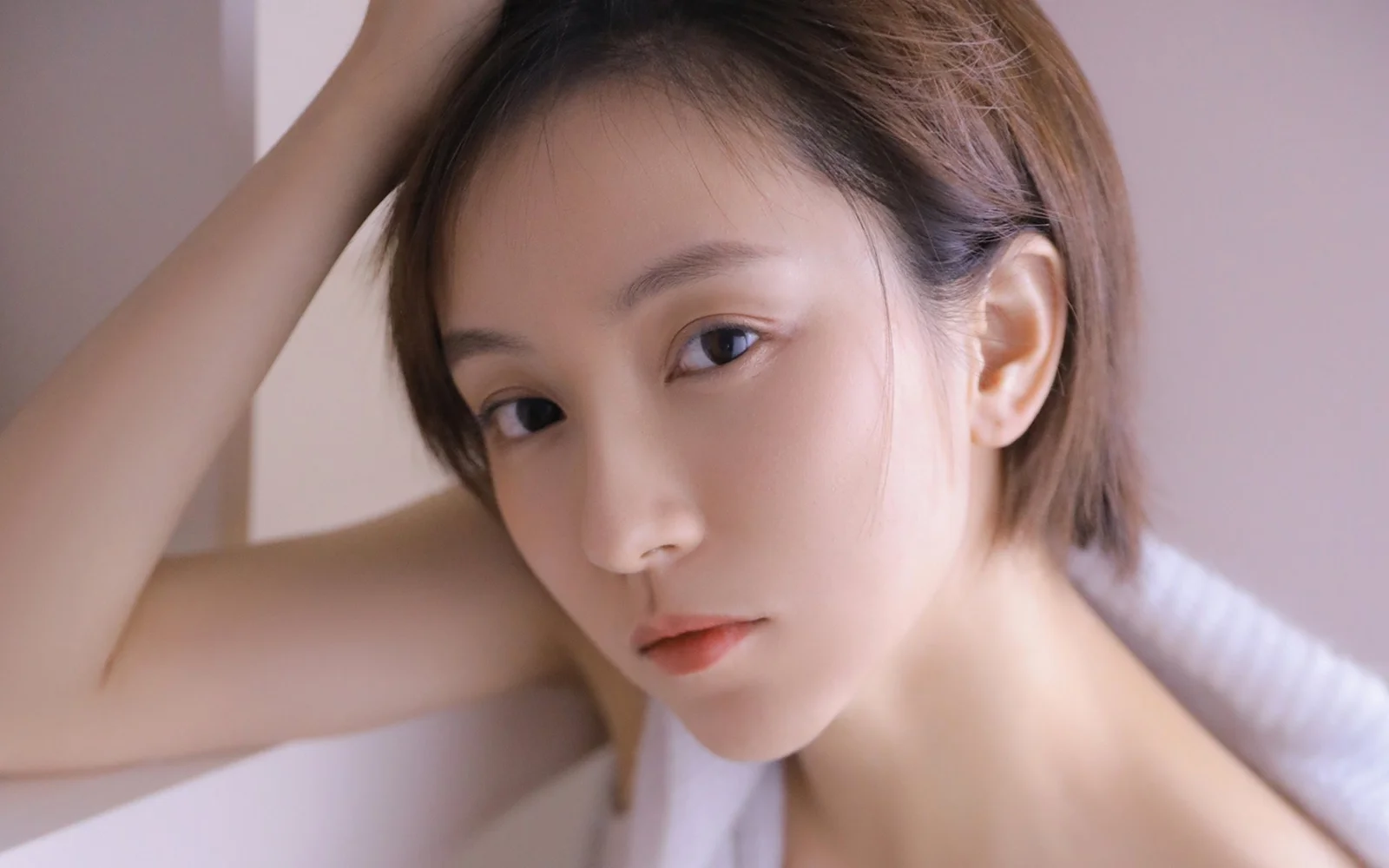 柔らかな室内光の中で、成人女性がカメラの近くで頭の横に腕を上げてポーズを取っている。