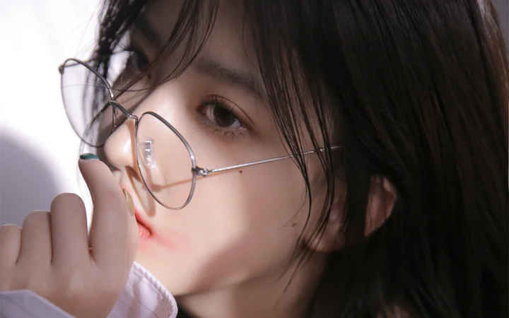 一名戴圆框眼镜的女性侧脸近距离面对镜头，手指轻触眼镜边缘。
