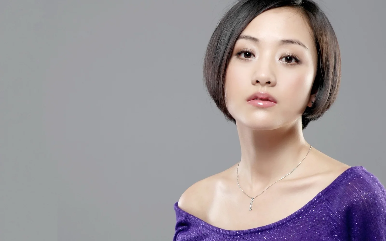 一名短发女性身穿紫色露肩上衣，在灰色背景前进行棚拍肖像。