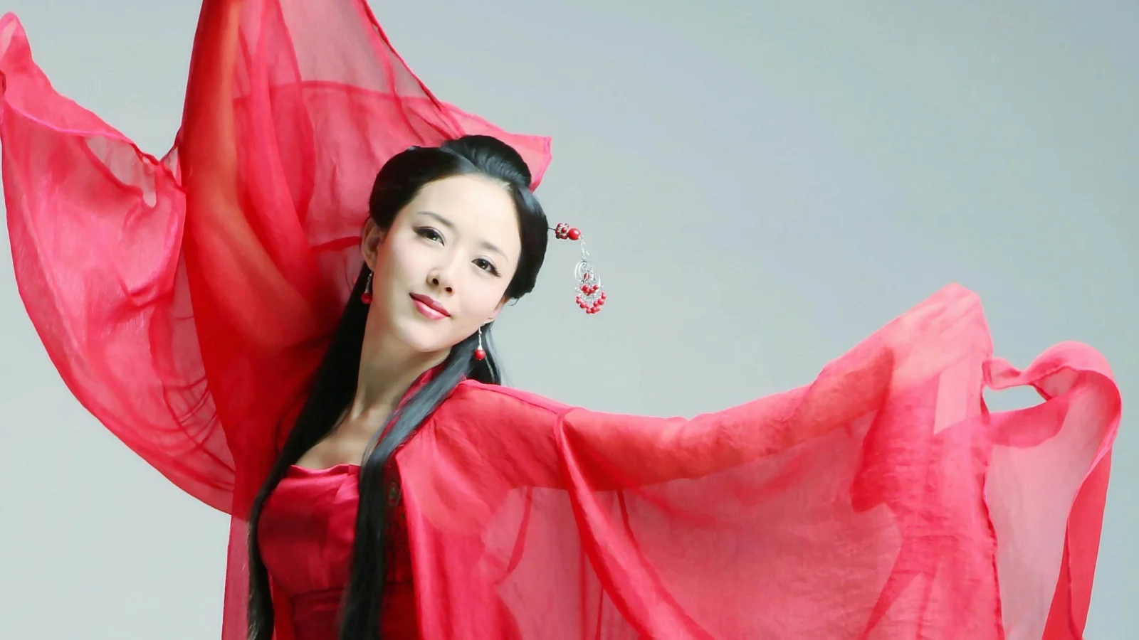 一名成年女子身穿红色传统服饰，在浅灰色背景前展开飘逸衣袖。
